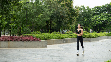 Fototapeta premium Happy woman listening music on earphones while running in nature in the morning. Healthy fitness woman jogging outdoors.