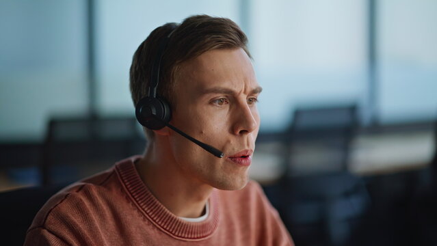 Serious helpdesk assistant talking headset in office coworking space closeup