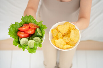 Mom-to-be comparing fresh vegetable plate with processed chips. Real-life moment of nutritional...