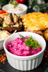 Assorted festive dishes on a table, including beet salad with herbs, sardine toast, creamy appetizers, and baked cheese casserole. Traditional Eastern European holiday food
