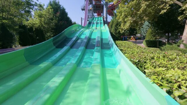 Two kids racing down parallel water slides on blue mats at a water park. Action-packed summer moment full of fun, laughter, and speed under the sun