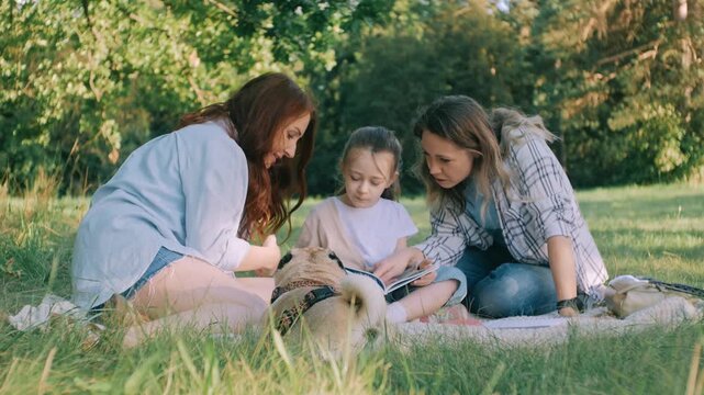 Friends are relaxing in nature. Two women, a child, and their dog came to relax in nature. The girl is reading a book.