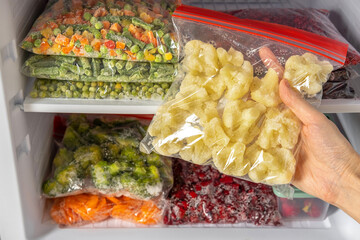 Female hands retrieving frozen cauliflower from freezer. Plastic bags with different frozen vegetables and berries in refrigerator.  Winter supply food in zip bags, preserving nutrients.