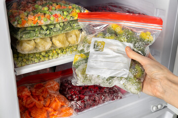 Female hands retrieving frozen broccoli from freezer. Plastic bags with different frozen vegetables and berries in refrigerator.  Winter supply food in zip bags, preserving nutrients.