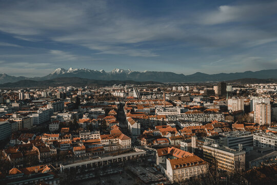 A panoramic view of the city of Ljubljana, with its red roofs and historic architecture, set against the majestic, snow-capped Julian Alps.  - Powered by Adobe