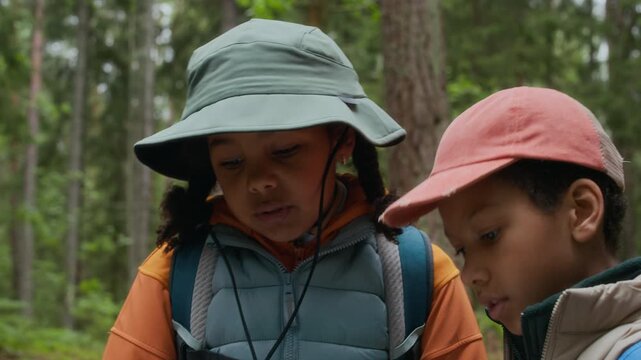 Two African American kids exploring forest while reading map, learning navigation skills and enjoying adventurous hike in nature