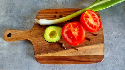 Kitchen home with food preparation, wooden board with tomatoes, green onions, avocado and allspice on gray table. Proper nutrition concept.