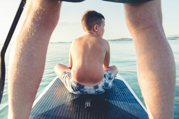 Photo of father and son enjoying their summer adventures. A man and a cute boy paddleboard on a clear blue ocean. They glide effortlessly on a blue surfboard, enjoying the sunny day.
