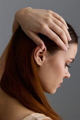 Naklejka premium beauty woman with red hair and flawless skin posing gracefully with hand on head against neutral gray background, showcasing elegance and natural style
