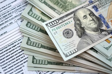 Big amount of United States hundred dollar bills in bunch on table with tax return form