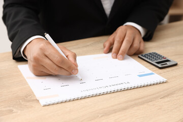 Man using business planner at wooden table in office, closeup