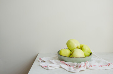 Organic green Antonovka apples from farm in a plate on natural stone countertop. Fresh healthy fruit in bright kitchen.
