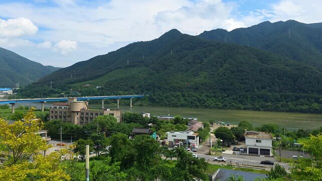 An aerial panorama soars above the Bukhangang River in Gapyeong, capturing bustling traffic on the Sincheongpyeongdae Bridge and the impressive Cheongpyeong Dam nestled among verdant mountains