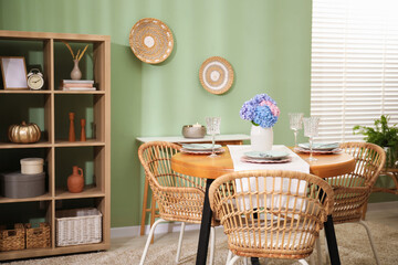 Stylish setting with plates and vase of flowers on wooden table in dining room. Interior design