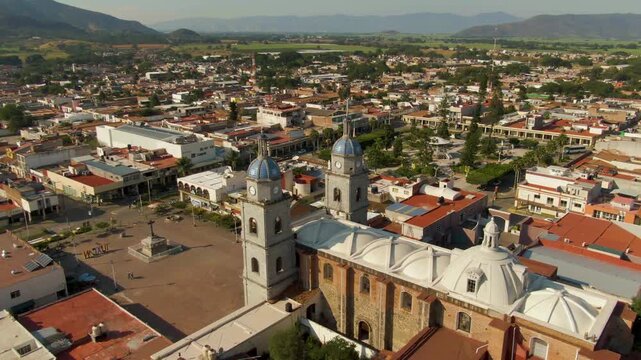 Drone orbit around twin- owered San Juan Bautista temple overlooking town plaza, surrounding rooftops, and distant hills