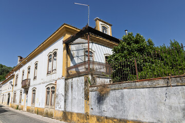 A weathered, traditional Portuguese building with peeling yellow and white paint stands under a clear blue sky, showcasing its rustic charm and historic character.