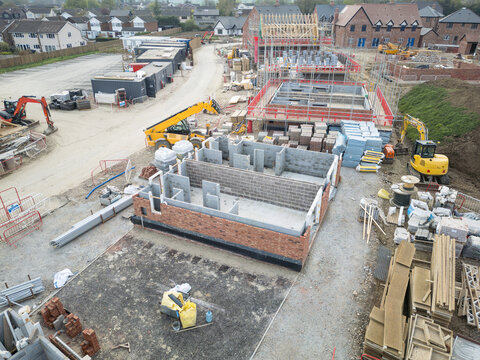 Unique, aerial view of a newly started construction of starter homes within a housing project in rural Britain. Older houses of the village are in the background.