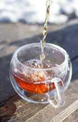 Hot tea being poured into clear glass cup with steam rising