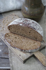 Round loaf of rustic bread cut in half with wheat grains on board
