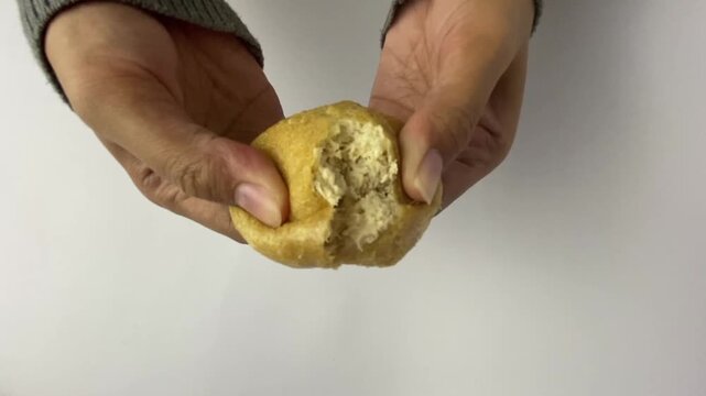 Hands splitting tahu bulat or fried round tofu, isolated on white background.