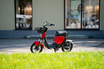 Red electric scooter with basket parked on urban street near building, showing modern eco-friendly...