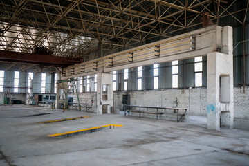 Large empty industrial warehouse interior with concrete floor, steel roof trusses, and daylight windows, representing logistics infrastructure, factory space, and industrial architecture