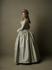 Fototapeta premium Elegant young woman from the 1700s Early Rococo era in ivory silk gown with fitted bodice and voluminous hairstyle, back three-quarter view portrait