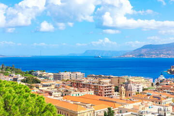 Obraz premium Colorful rooftops and historic buildings line Messina scenic coastline, overlooking blue waters of Strait of Messina in Sicily. Sky and distant mountain highlight city vibrant Mediterranean atmosphere