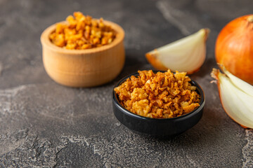 Crispy fried onions in a bowl on a wooden table. Roasted Onions. Seasoning for dishes. Spices. Salad dressing. Space for text. Copy space