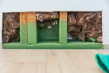 Drywall section removed revealing intact wood framing and insulation in a residential wall, green painted base structure with no visible water damage