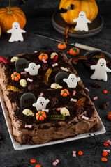 Halloween chocolate cake. Dirty cake with chocolate cream, decorated with worms, skulls, ghosts, pumpkins and sugar sprinkles on a dark background.