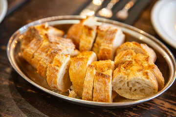Tray of sliced French baguette with golden crust and soft interior served on silver plate, rustic bread presentation in cozy restaurant setting