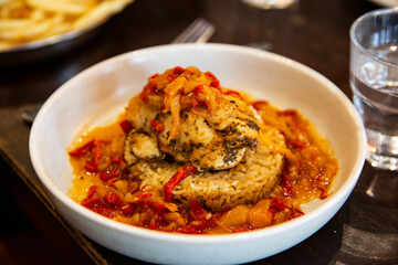 Grilled chicken breast with spiced seasoning atop seasoned rice, surrounded by stewed red peppers and onions in a flavorful sauce, served in deep bowl