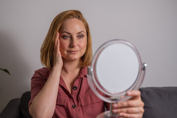 Portrait of middle age woman looking at mirror touching her skin, aging, skin care