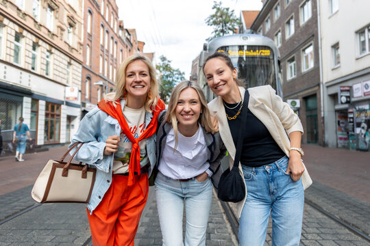 Three cheerful young adult women friend walk street old european german Hannover city street enjoy having fun laughing sunny day together. Female persons friendship celebration party weekend