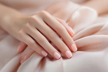 Delicate hands display a classic French manicure, featuring clean lines and a subtle sheen. The nails complement the soft silk fabric beneath, creating a calming aesthetic