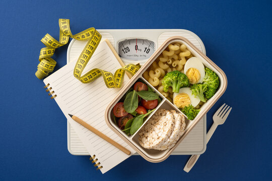 Balanced meal preparation featuring vegetables, a notebook, a scale, and measuring tape, symbolizing a healthy lifestyle, fitness, and weight management