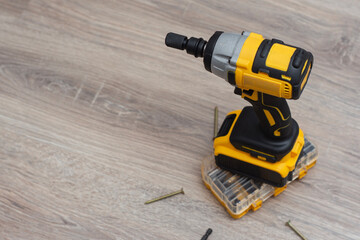 Cordless impact wrench on a wooden surface, accompanied by screws, drill bits, and a storage case. Electric tools for construction and DIY projects.
