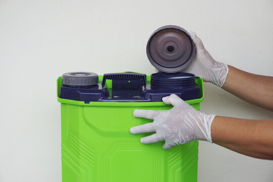 Hands wear protective gloves, carefully opening the black cap of a green chemical sprayer tank. Concept,safety awareness, proper handling of hazardous substances, and agricultural training.     
