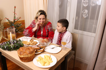 Mother and son in embroidered shirts celebrate Christmas at the table in a warm festive atmosphere and preserving Ukrainian traditions.