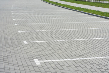 Car parking made of paving stones and markings with sidewalk and grass.