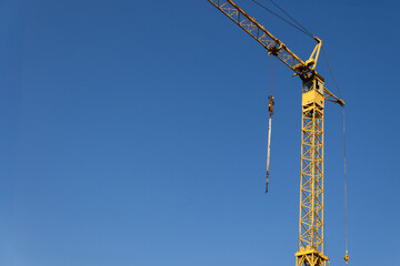Naklejka premium A bright yellow tower crane stands tall against a clear blue sky, ready for construction work. This heavy machinery is essential for lifting materials on a building site.