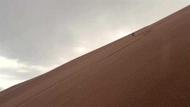 Person running down the Great Sand Dunes National Park Sangre de Cristo range Rocky Mountains spring summer raining cloudy Colorado unique magical large amounts of sand dune hills windy landscape