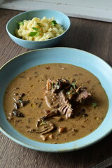 Top view of a traditional Czech dish — beef with mushrooms — served on a blue plate. A delicious autumn meal, rich in flavors, featuring tender beef pieces in a creamy mushroom sauce, food background