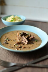 Close-up view of served beef with creamy mushroom sauce on a blue plate, rustic wooden table background.