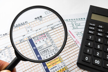確定申告書と電卓、虫眼鏡を使った税金計算イメージ