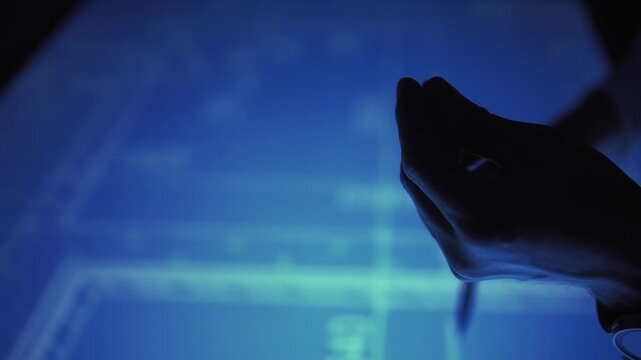 Silhouette of male hands with stylus over blueprint on a large touch screen
