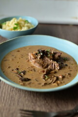 Daily menu with a traditional autumn dish — beef with mushroom sauce served on a blue plate. A hearty Czech-style meal with tender beef, pasta, and mushrooms, presented in a rustic homemade style