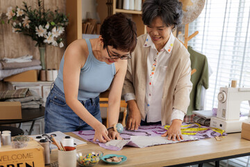 two Asian women collaborating in their clothing design studio.