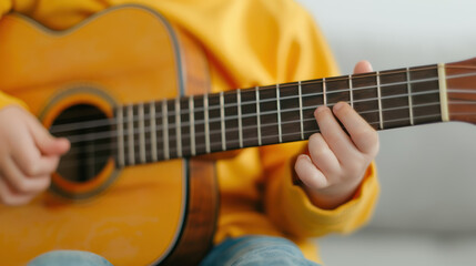Fototapeta premium A child plays a guitar, focusing on the strings while wearing a bright yellow sweater, showcasing a moment of musical engagement and creativity.